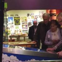 A man stands in front of a pinball machine while another man and woman watch him play